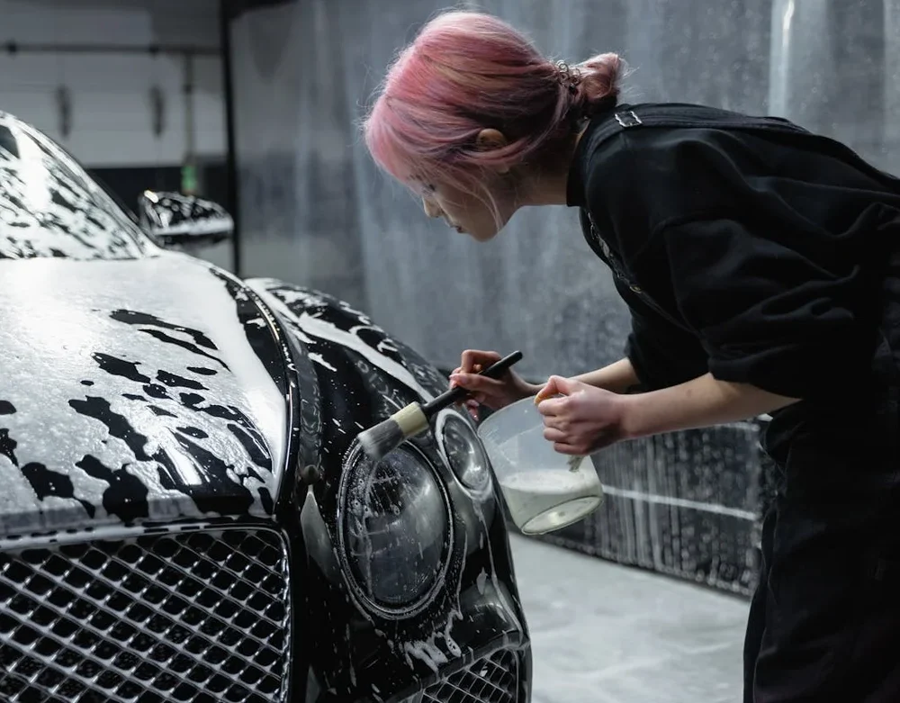 Persona lavando a mano un coche negro cubierto de espuma