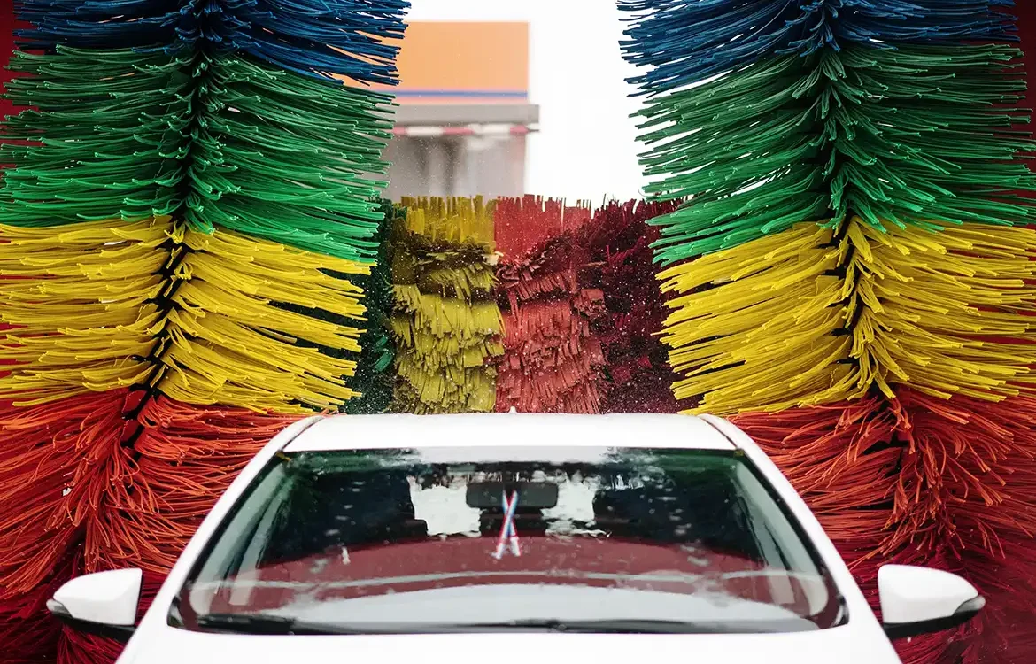 Coche blanco entrando en un túnel de lavado con rodillos de colores
